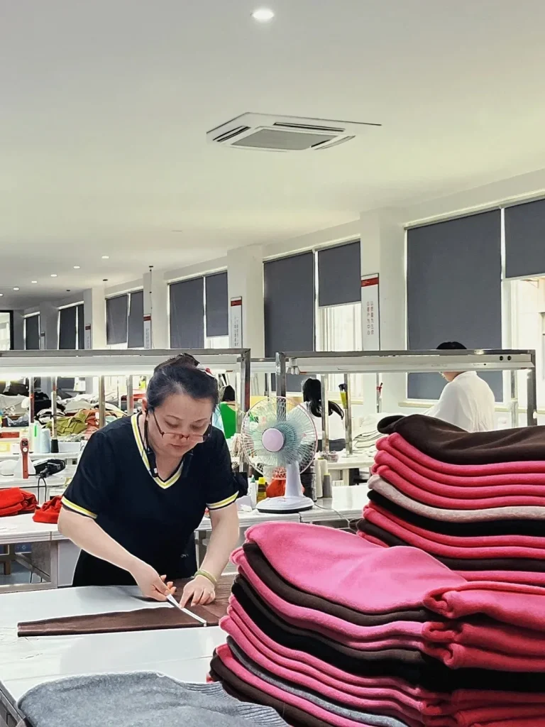 QC workshop real shot, worker measures multi-color anti-pilling premium knit sweaters, strict finished garment dimension & appearance inspection factory photo