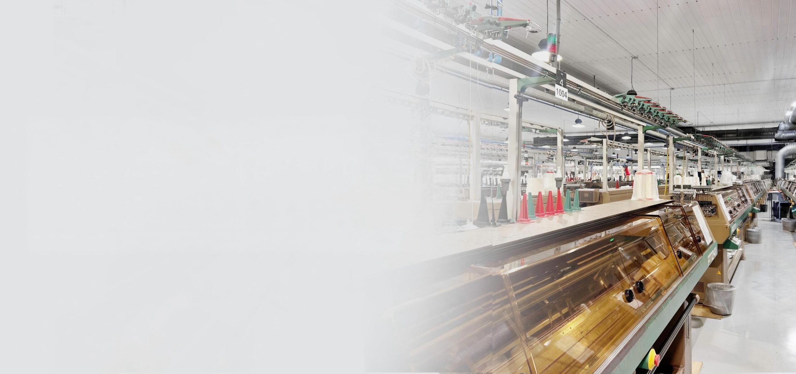 Left faded wide banner background of full-auto computer flat knitting machine production line, large workshop panoramic photo for custom sweater manufacturer website header
