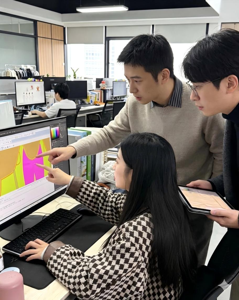 Modern office real shot of OEM knitwear design team, designers collaborate on custom garment pattern & color scheme via CAD software, original style development workflow photo