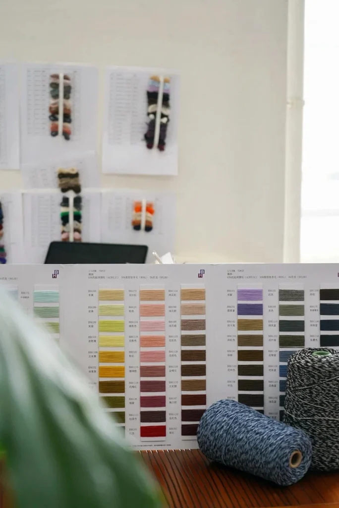 Factory supervisor inspects premium alpaca knit sample against tech pack & yarn swatches on workstation, high-end knit OEM quality control & traceable production workshop photo