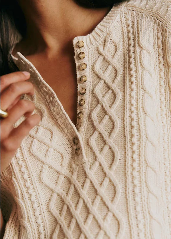 Close-up texture shot of cream 100% twisted organic cotton henley cable knit top, detailed diamond cable stitch & wood button placket, textured sustainable cotton knit detail marketing photo