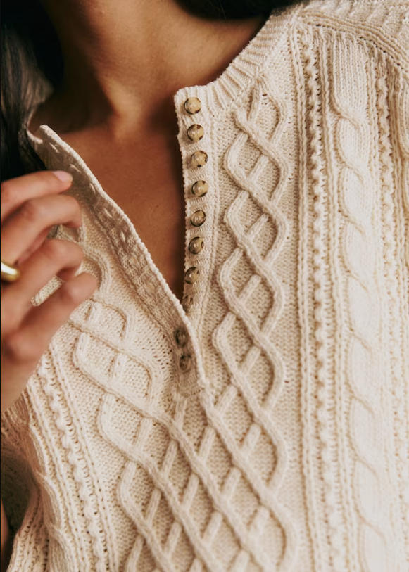 Close-up texture shot of cream 100% twisted organic cotton henley cable knit top, detailed diamond cable stitch & wood button placket, textured sustainable cotton knit detail marketing photo